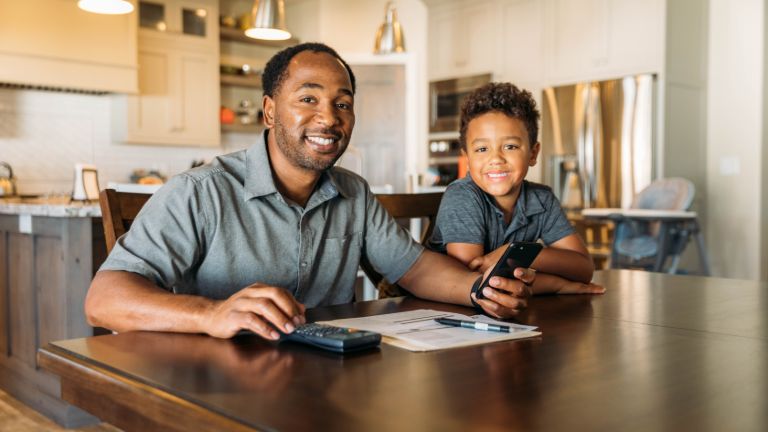 Smiling father and son at a table with a calculator and paper.