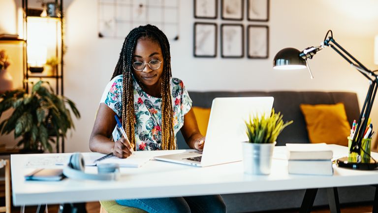 Woman sitting at a desk with a laptop and taking notes