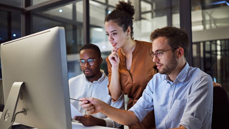A team of three professionals sitting at a computer together discussing a topuc